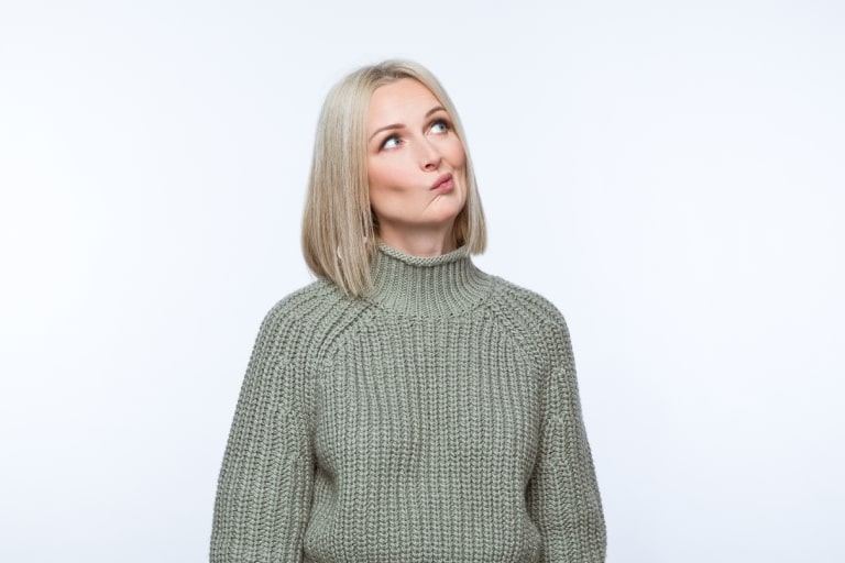 Portrait of cconfused mature woman wearing khaki sweater, looking away. Studio shot, grey background.