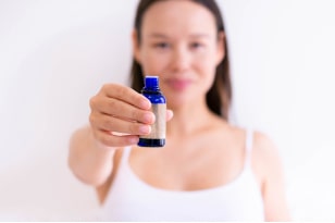 A pretty healthy young woman holding a small glass bottle, smiling with a white background.