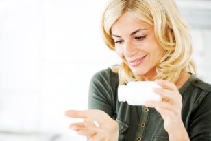 Young blonde woman is holding a pill bottle and a pill in her hand. The focus is on the blonde woman.