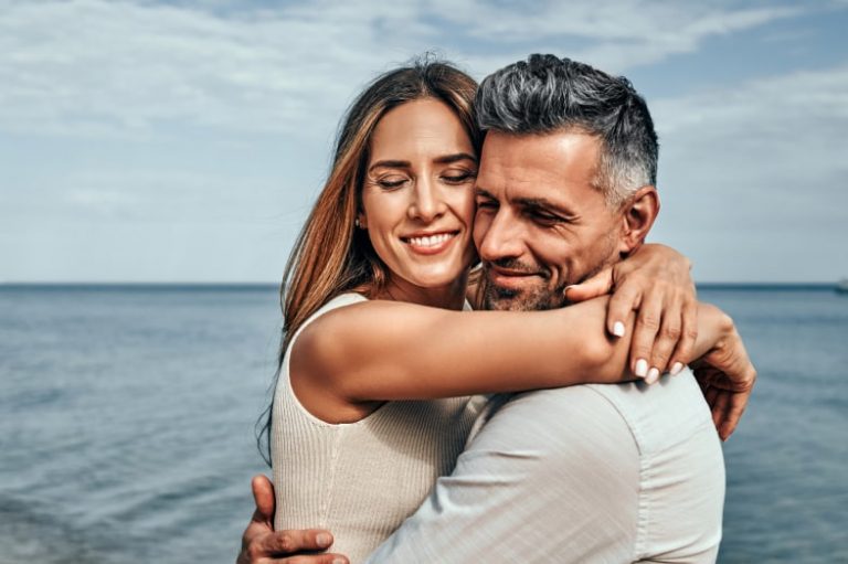 Close up view of a portrait of a handsome couple in love hugging while walking along the beach