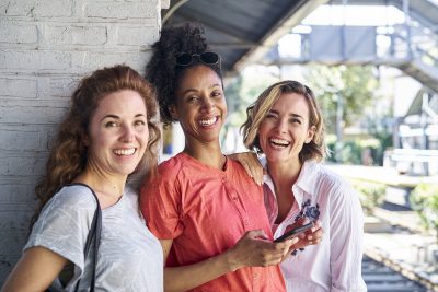 Female friends holding smart phone standing at train station