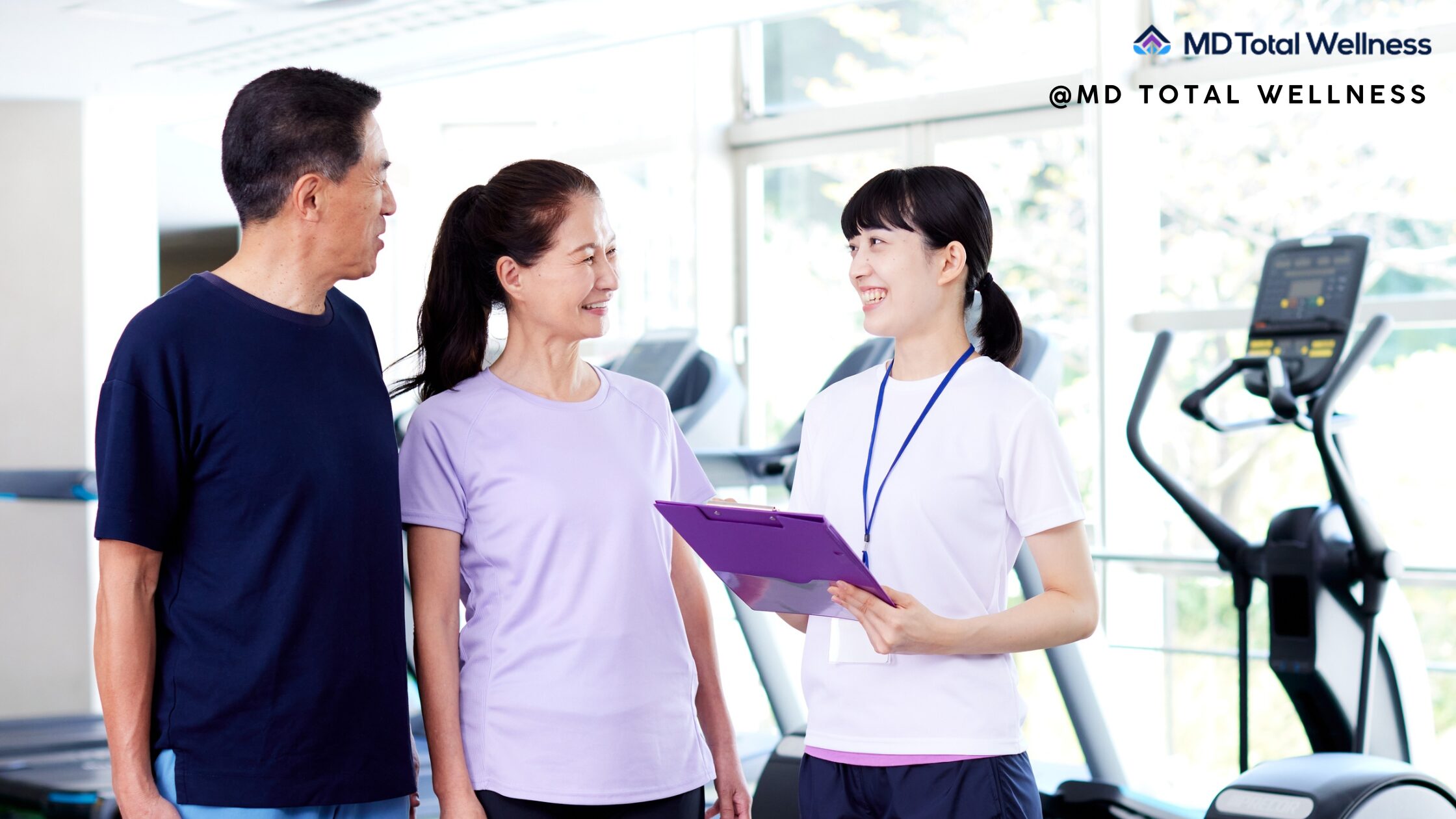 A fitness trainer in A fitness trainer with clipboard consults with a smiling couple in workout clothes at a modern gym facility with clipboard consults with a smiling couple in workout clothes.